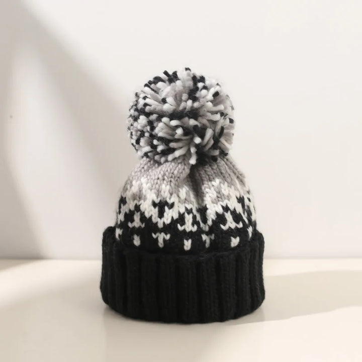 Women's cozy knitted winter beanie hat with white snowflake pattern & fluffy pom-pom.