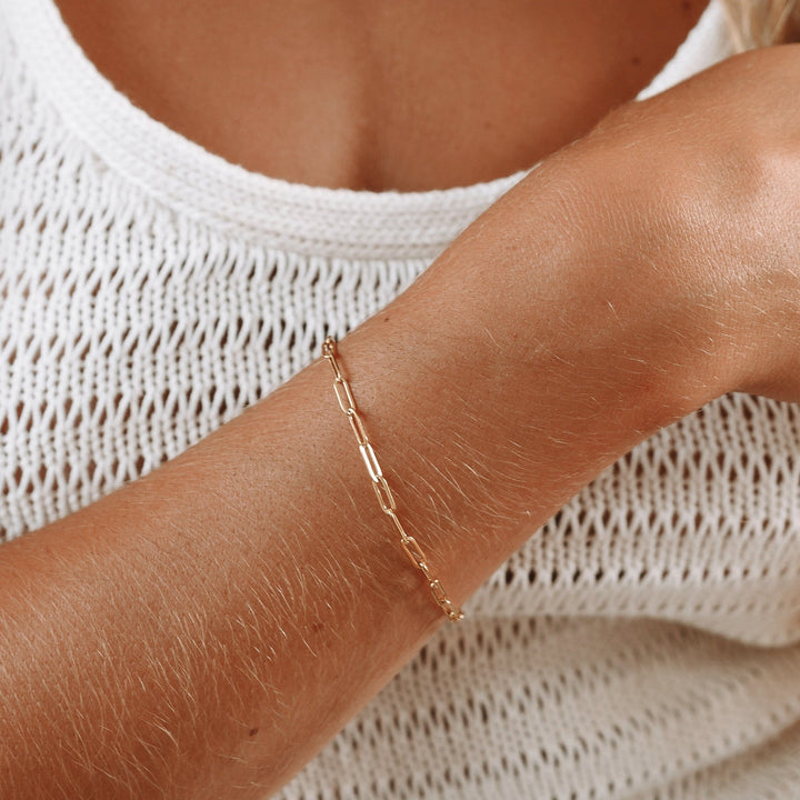 Close-up of a women's gold paperclip link chain bracelet. Dainty, hypoallergenic & adjustable for a perfect fit.
