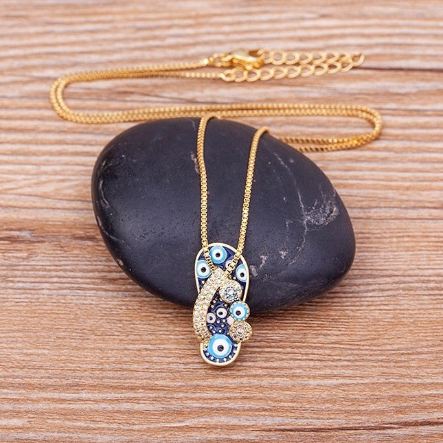 Fashionable women's gold necklace with a detailed flip flop and an iridescent evil eye pendant, ideal for summer style.