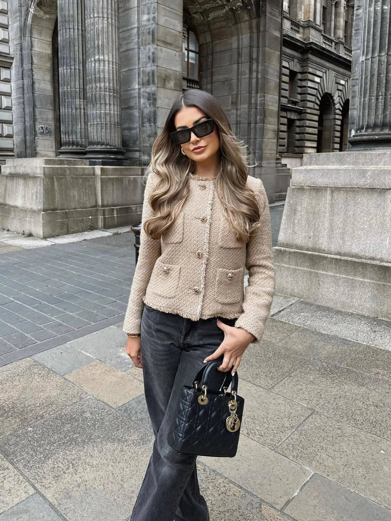 Close-up of a women's elegant beige tweed jacket, showcasing detailed tweed texture and prominent gold buttons.