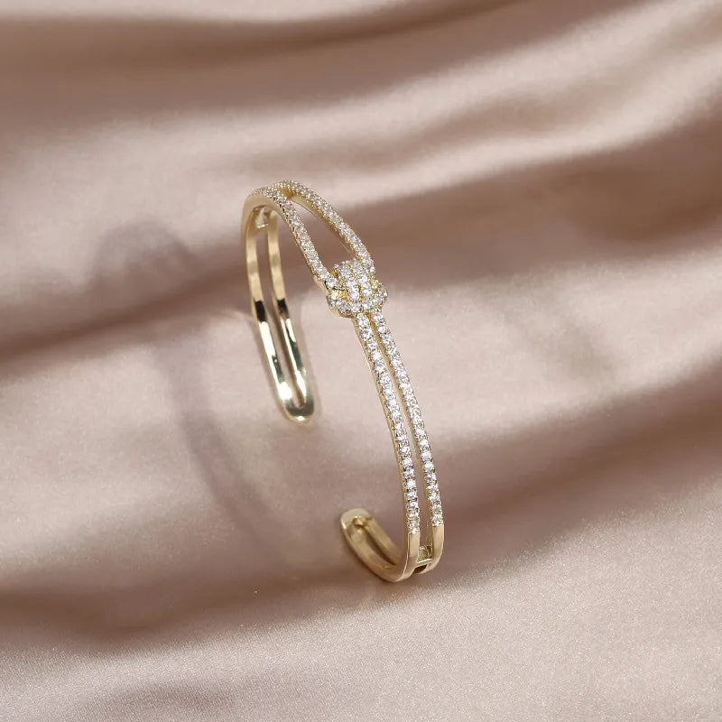 Sparkling gold metal knot bangle bracelet adorned with crystals for women.