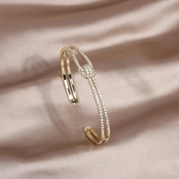 Sparkling gold metal knot bangle bracelet adorned with crystals for women.