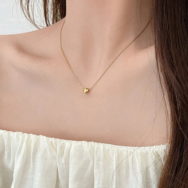 Woman wearing a sleek minimalist heart necklace, elegant gold-tone dainty jewelry, perfect for everyday.