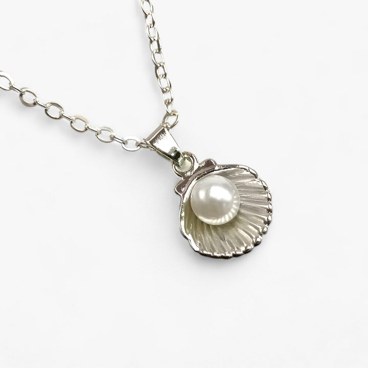 Close-up of a women's ocean charm necklace with lustrous pearls, delicate seashells, & a silver-tone chain.