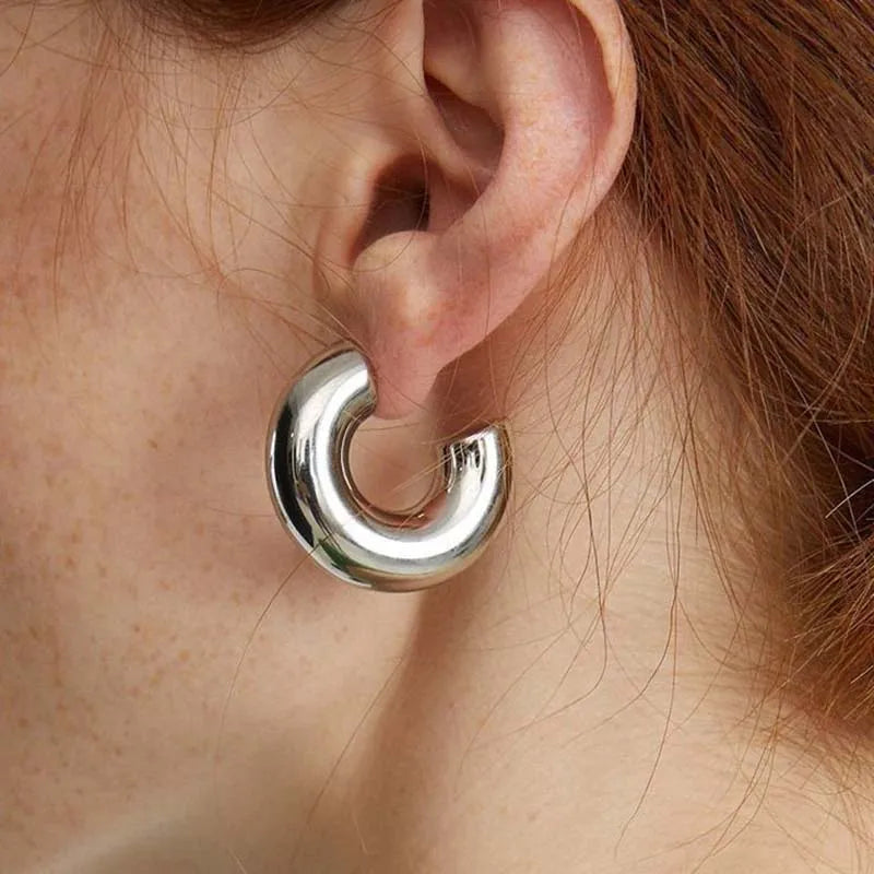 Close-up of women's polished sculptural hoop earrings. Gold & silver finish, elegant fashion accessory.