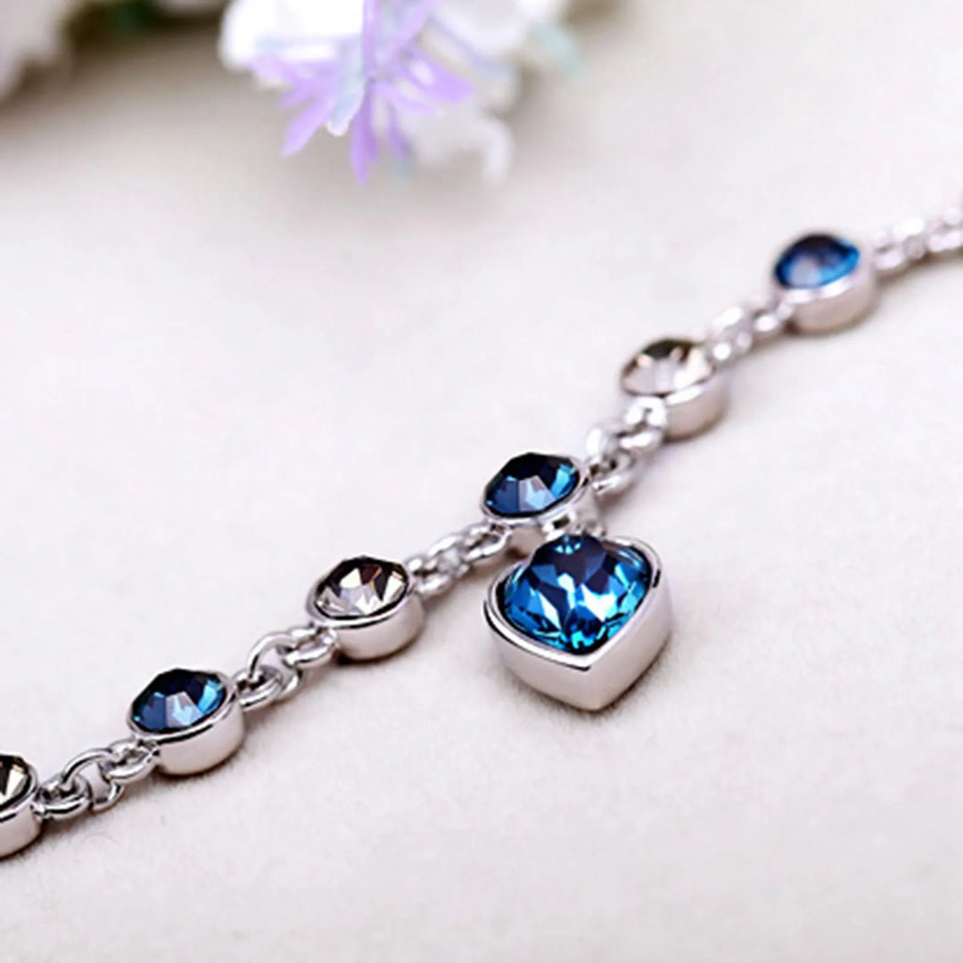 Close-up of women's Heart of the Ocean crystal bracelet, detailed sparkling blue heart & silver chain.