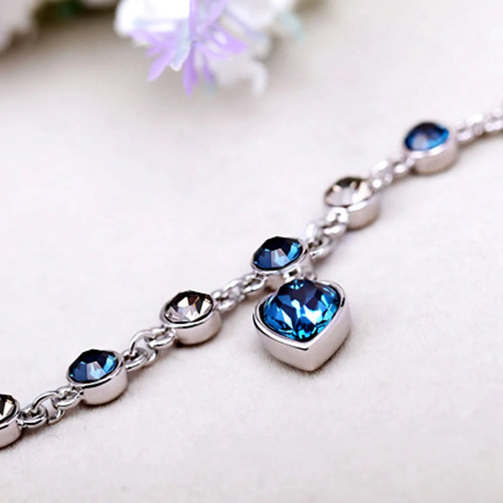 Close-up of women's Heart of the Ocean crystal bracelet, detailed sparkling blue heart & silver chain.