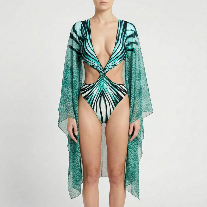 Model wearing a women's abstract print long-sleeve cutout monokini swimsuit on a sunny beach.