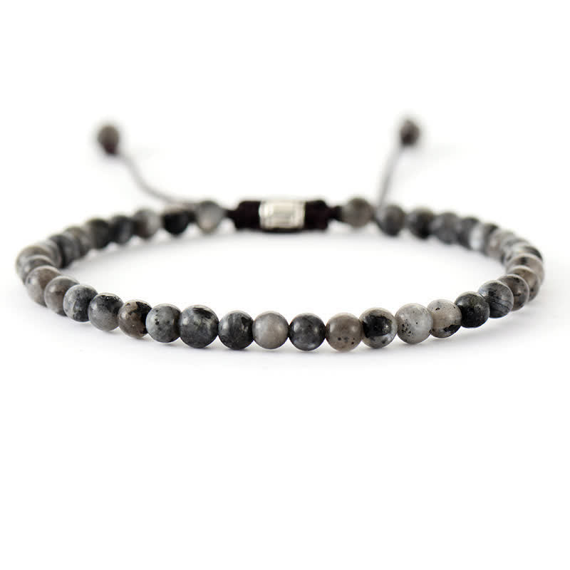 A stack of women's natural stone and pearl adjustable braided bracelets on a wrist. Boho chic.