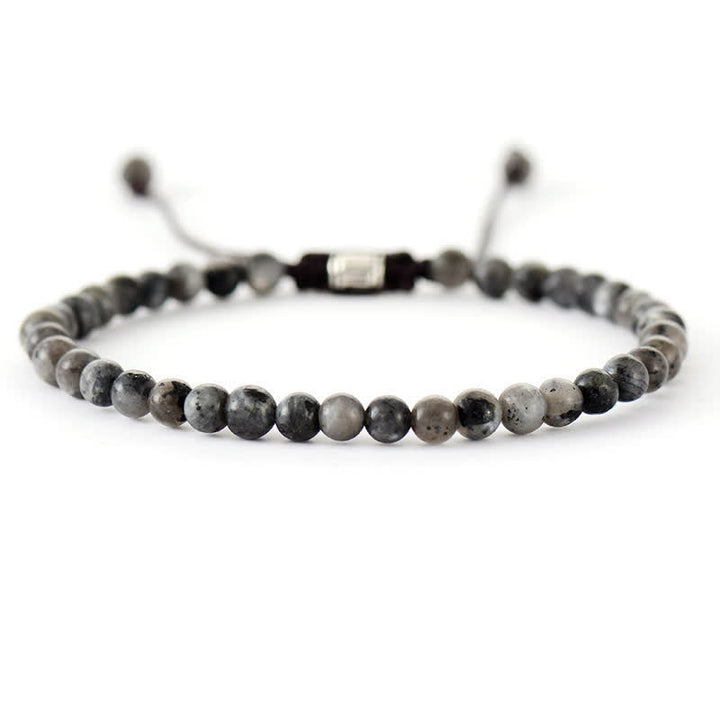 A stack of women's natural stone and pearl adjustable braided bracelets on a wrist. Boho chic.