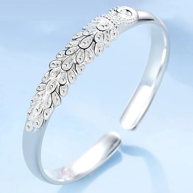 Detailed sterling silver peacock charm on a women's charm bracelet, elegant animal jewelry.