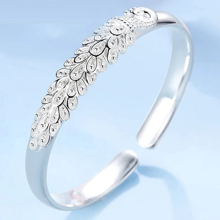 Detailed sterling silver peacock charm on a women's charm bracelet, elegant animal jewelry.