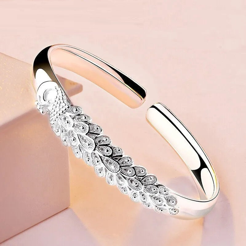 Close-up of a shimmering sterling silver peacock charm on a women's bracelet, unique animal jewelry.