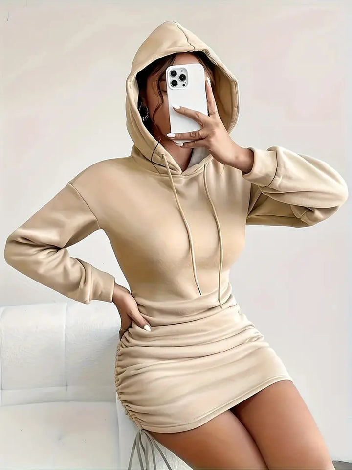 Model wearing a black versatile women's hoodie dress. Adjustable ruched sides create a flattering fit.