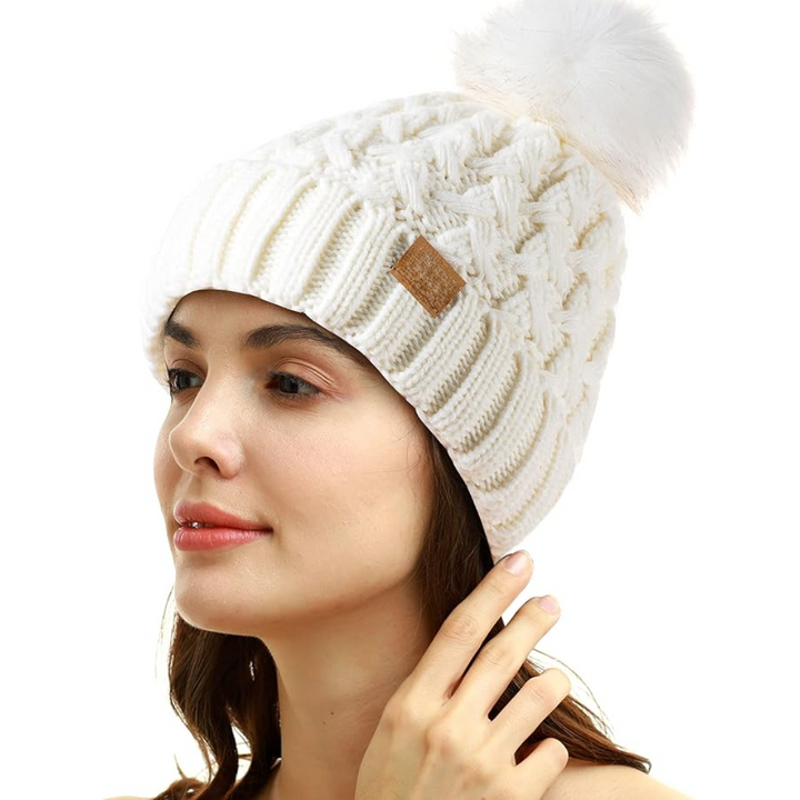 Close-up of a comfortable orange cable-knit women's beanie with a stylish faux fur pom.